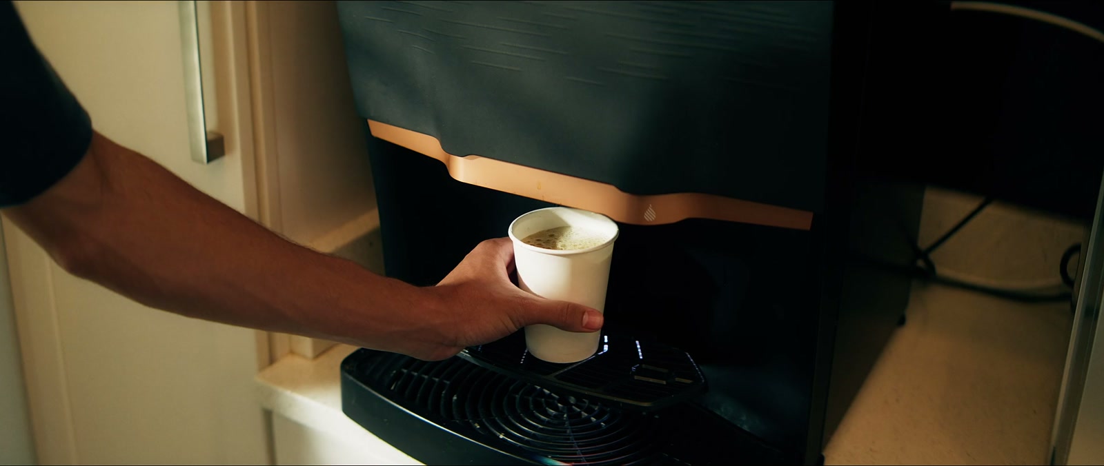 Hand taking a fresh cup of coffee from a bean-to-cup machine